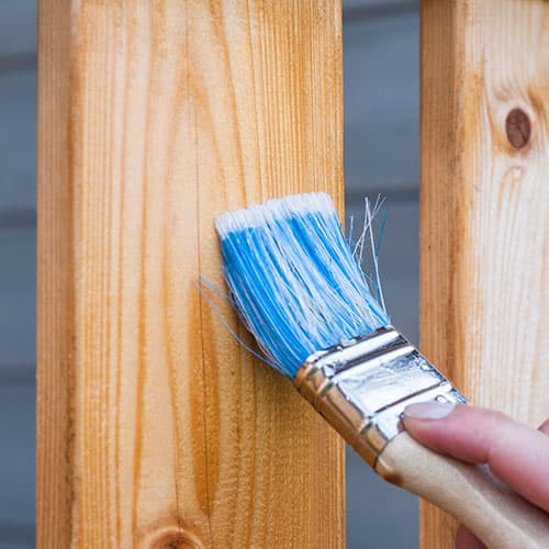 Close-up of a brush applying fresh paint to wood exterior siding
